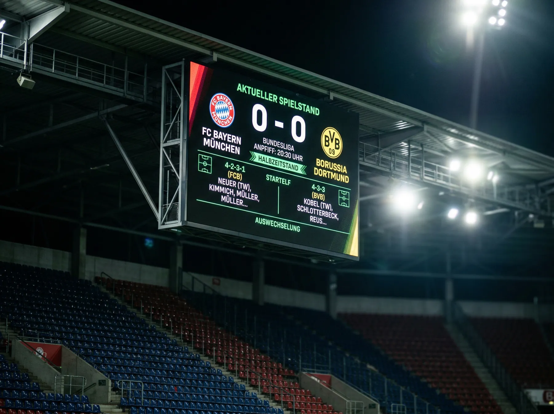 Elektronische Anzeigetafel in einem Fussballstadion mit Spielstand und Mannschaftsaufstellungen während eines Abendspiels